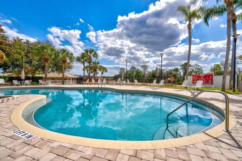 Outdoor pool area with lounge chairs and palm trees under a partly cloudy sky