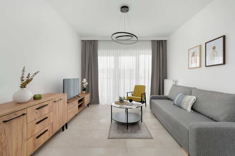 The spacious living room is furnished with a long wooden media console and a matching storage unit. A grey sofa and a yellow accent chair offer ample seating around a central coffee table.