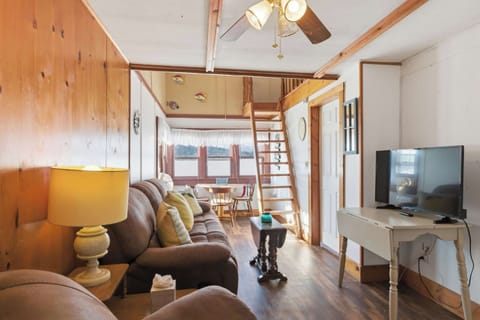 The living room opens all the way through to the lakeside dining nook, with the loft ladder tucked in the corner and warm knotty pine wrapping the whole space.