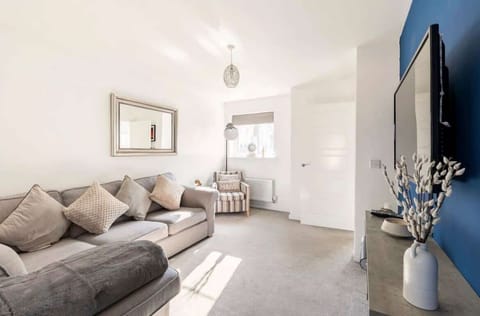 Relax in a bright, modern lounge with a plush sectional, cozy armchair, and calming blue accents. Natural light, stylish décor, and a sleek TV wall create the perfect space to unwind after exploring the city.