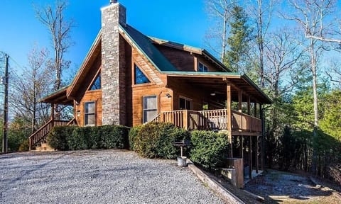 Beautiful mountain cabin with stone chimney and wraparound deck, nestled among trees with convenient parking area.