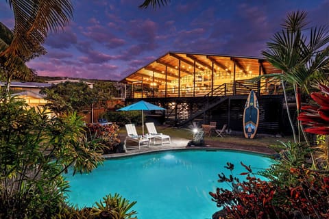Modern tropical retreat with stunning architecture illuminated against a dramatic purple sky, featuring a pristine pool and lush garden setting.