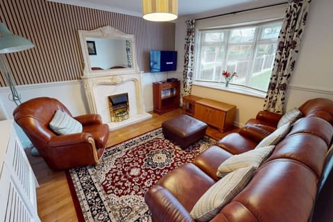 The living room provides seating for multiple guests around a fireplace with an ornate white surround, with a bay window bringing natural light into the room.