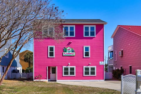 Bright pink vacation rental building with colorful signage creates a cheerful beachside atmosphere in this coastal neighborhood.
