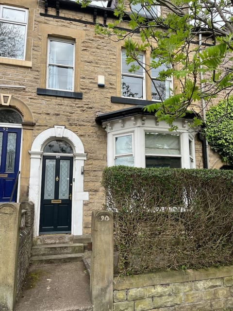 The stone-fronted Victorian terraced house exterior shows a blue front door, bay window, stone front steps, and a hedge-lined boundary wall.