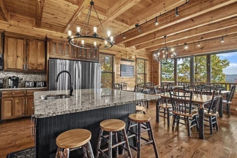 An open-concept kitchen and dining area with expansive windows, statement lighting, and a large island with bar seating. Thoughtfully designed for shared meals, conversation and enjoying Smoky Mountain views.