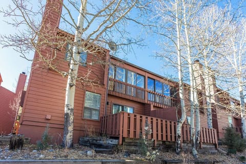 Charming mountain retreat with distinctive red-brown siding and multi-level balconies, nestled among bare aspen trees in a peaceful winter setting.