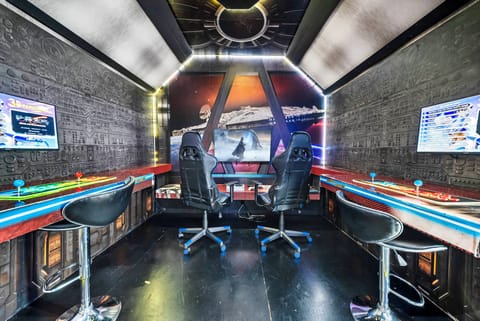 Experience a one-of-a-kind gaming hub with sleek black walls and vibrant LED lights that enhance the ambiance. Enjoy thrilling gaming sessions with friends on dual screens while relaxing on stylish bar stools.
