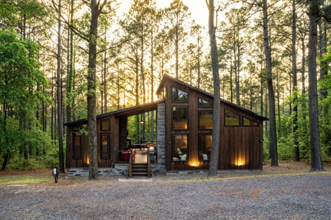 Showcasing a combination of stone and wood architecture, this cabin offers a welcoming entrance with its expansive porch and open design. Beautiful uplights and floodlights illuminate the exterior at night.