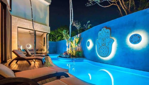Illuminated private pool at night with glowing Hamsa hand wall art and tropical garden ambiance.