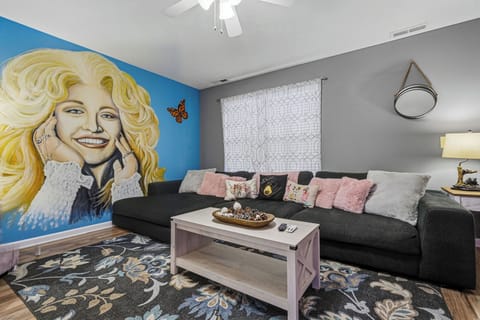 Relax in your stylish living room with plush seating, a bold mural, and touches of pink and gray that create a warm, welcoming atmosphere.