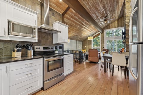 Gather around this stunning open-concept kitchen where exposed wooden beams create rustic charm above modern appliances and white cabinetry.