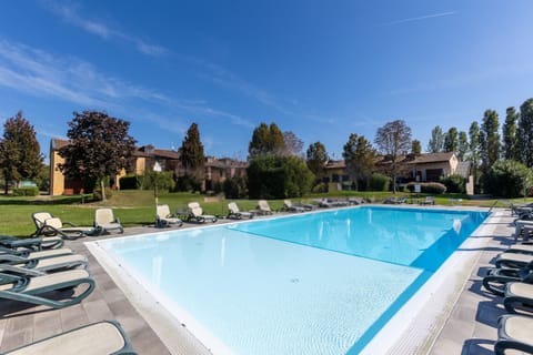 Apartment with a pool in Castelnuovo del Garda, surrounded by spacious green areas and a relaxation area with lounge chairs. The property is strategically located near Lake Garda’s main amusement parks, such as Gardaland, Movieland, and Caneva Aquapark, making it ideal for family vacations.