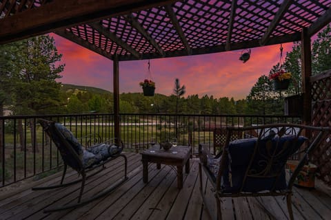Rock back in wrought-iron chairs under the pergola, hanging flower baskets swaying as the mountains stretch out beyond the rail. - Pergola Deck Seating - The Alta - Angel Fire, NM