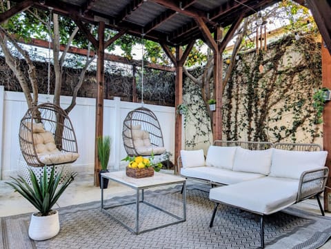 This private, gated, and completely secluded covered patio offers total peace of mind with handy driveway access. A rustic, solid-roofed wooden pergola shelters a grill, sleek sectional, plush cushions, and twin hanging teardrop swings.