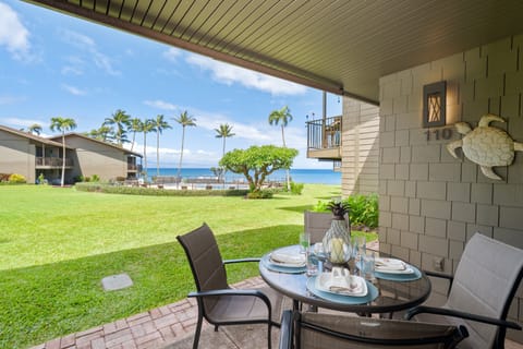 Ground-floor oceanfront lanai with dining set and lush lawn views.
