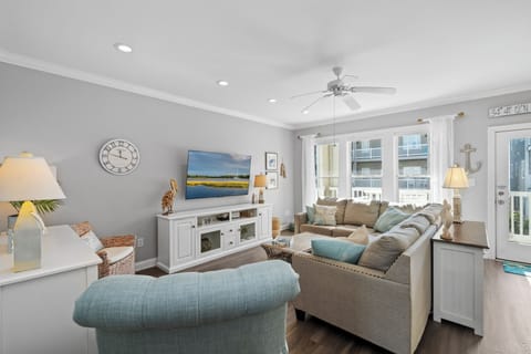 Relax in your coastal-themed living room with plush seating, smart TV, and peaceful balcony views for perfect vacation evenings.