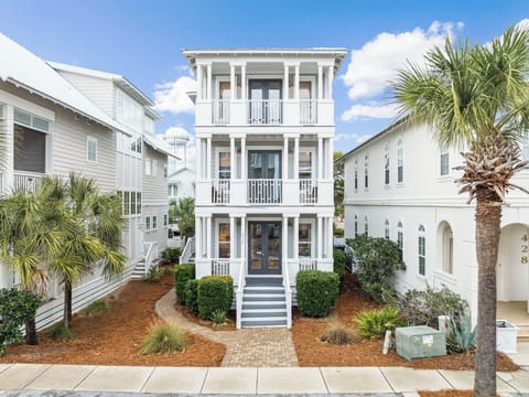 A charming three-story coastal home with white railings and palm trees in a peaceful neighborhood setting.