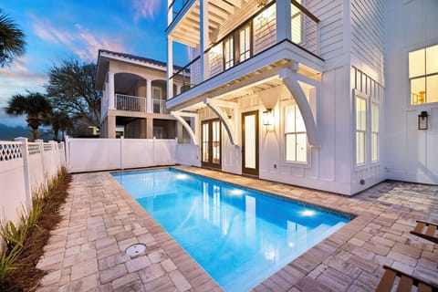 Elegant white coastal home featuring a private pool surrounded by stone pavers, tropical landscaping, and covered outdoor living spaces.