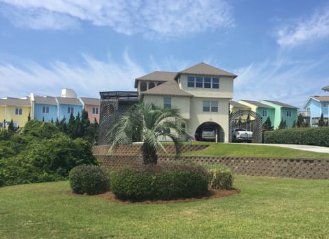 Coastal rental home featuring elevated architecture with ground-level parking and colorful neighboring beach houses creating a charming seaside community.