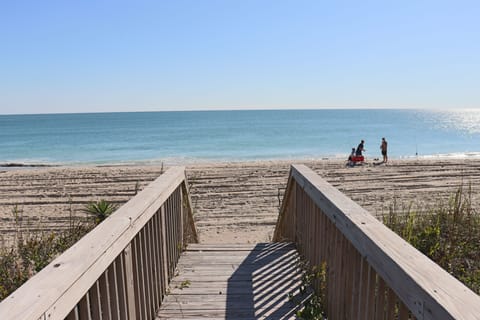 Pristine beach with wooden boardwalk leading to crystal-clear waters and soft sand where families enjoy peaceful seaside moments.