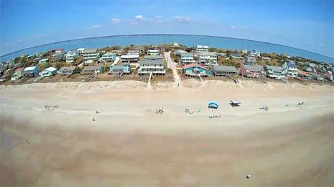 Stunning aerial view of the beachfront community with colorful homes dotting the pristine coastline and crystal-clear waters stretching to the horizon.