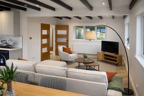 The spacious living room offers a bright and comfortable space to relax, featuring large windows that bring in natural light and views of the surrounding greenery. Stylish seating and a welcoming atmosphere make it the perfect place to unwind after a day exploring the Cornish coast.