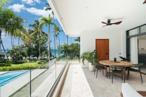 Outdoor dining area with a breezy balcony and partial ocean view. Enjoy meals with a sea breeze, overlooking the garden and pool below.