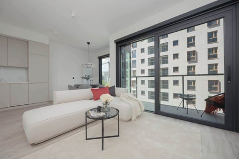 A bright living room with a large sectional sofa and access to a balcony. Natural light pours in through large windows.