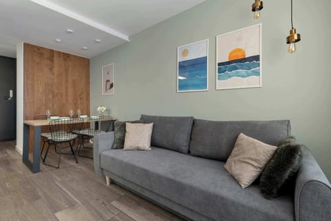 A stylish living room corner with a gray couch, wall art, and a wooden dining area in the background.