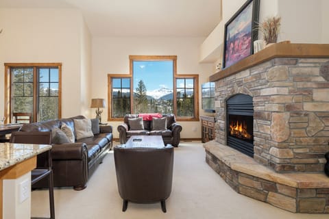 Cozy up by your stone fireplace while soaking in stunning mountain views through floor-to-ceiling windows in this inviting living space.
