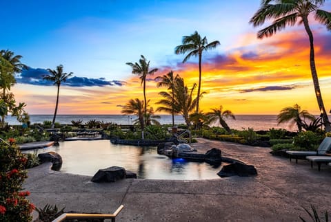 Swim beneath swaying palms in the lagoon-style pool, surrounded by tropical landscaping and cushioned loungers. HLI-7A
