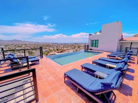 Relax on shared rooftop loungers beside a private pool with sweeping city views under clear blue skies