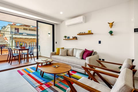Bright living room with a colorful rug, wooden coffee tables, and balcony access.