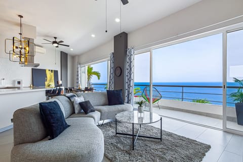 Bright, modern living space with floor-to-ceiling sliders opening to a stunning oceanfront balcony. Plush seating, sleek decor, and a smart TV make it perfect for relaxing with a view.