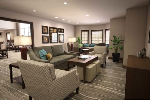 Hotel lounge with a gray sofa, patterned armchairs, and natural light filtered through wooden blinds