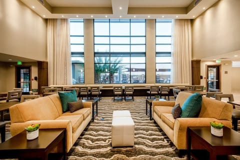 Sunlit lobby with beige sofas, blue accent cushions, and a communal table for guests