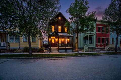 Welcome to Riverwalk Path! A mountain-style home glowing warmly at dusk, with board-and-batten siding, a covered front porch, and the colorful South Main streetscape setting the tone for your Colorado escape.