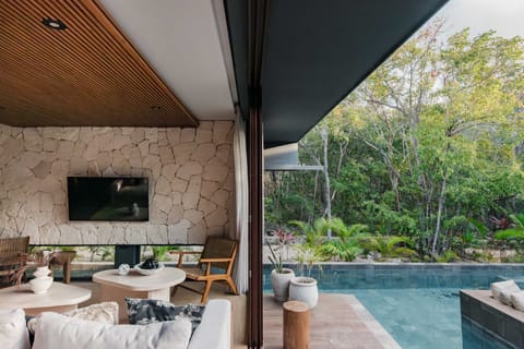 Living room with dark wood paneling, wall-mounted TV, and glass balcony doors to jungle.
