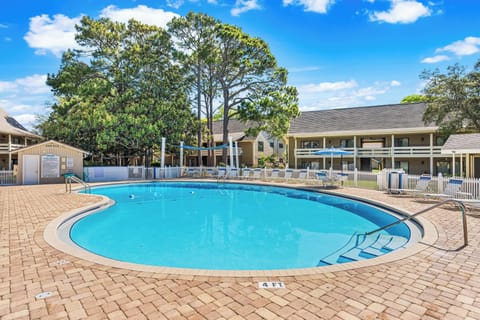 Sunny resort pool with brick surround, lounge chairs, and mature shade trees — a second home base on days off the beach