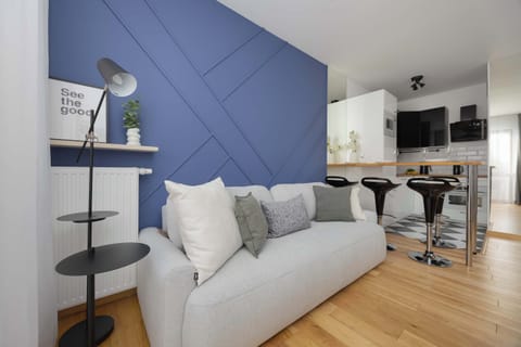 A cozy living area with a modern sofa and blue accent wall connected to a small dining space.