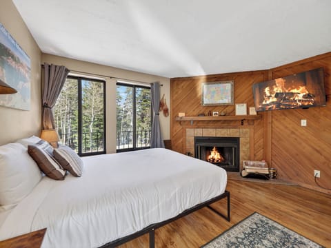 Cozy up in your mountain bedroom where crackling fireplace warmth meets forest views through your private balcony doors.