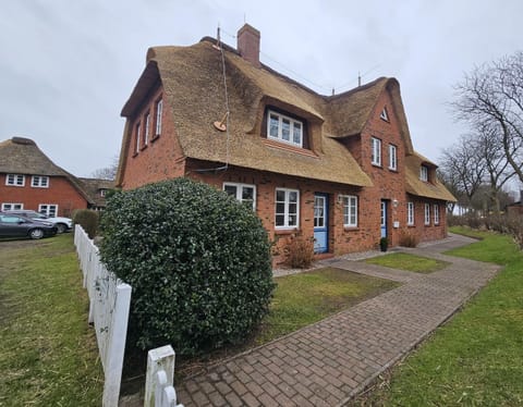 Exterior view of a thatched-roof house with a quiet garden.