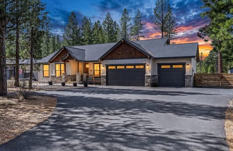 Modern mountain retreat with warm stone and wood facade, nestled among towering pines with spacious parking and dramatic sunset skies.