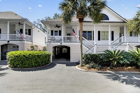 Classic coastal architecture features white railings, palm trees, and American flags in this charming property complex with covered parking.