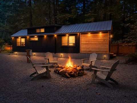 Gravel fire pit area with four gray Adirondack chairs surrounded by dark wood and cedar-paneled cabin exterior.