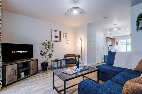 A modern living room with a blue sofa bed, sleek coffee table, and warm wood floors. Natural light, framed art, and greenery create a stylish yet cozy atmosphere, offering both comfort and extra sleeping space for guests.

