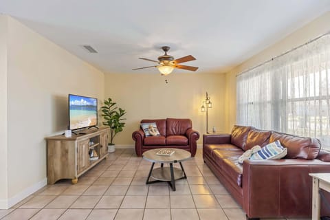 Relax in the cozy living room featuring leather sofas and a flat-screen TV with natural light from large windows.
