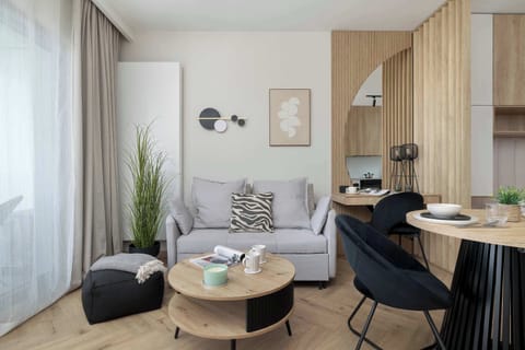 A stylish open-plan living area featuring a cozy sofa, a round coffee table, and a small dining space with dark chairs. Warm wood finishes and soft textiles create a welcoming and balanced interior.