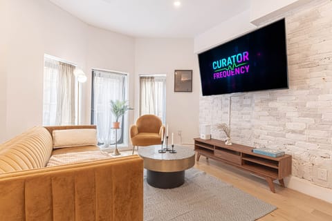 Bright living room with velvet sofa, brick wall, and large TV.